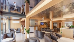 A modern hotel lobby with grey sofas, round tables, and a wooden reception desk. - Banana Guesthouse (Pattaya)