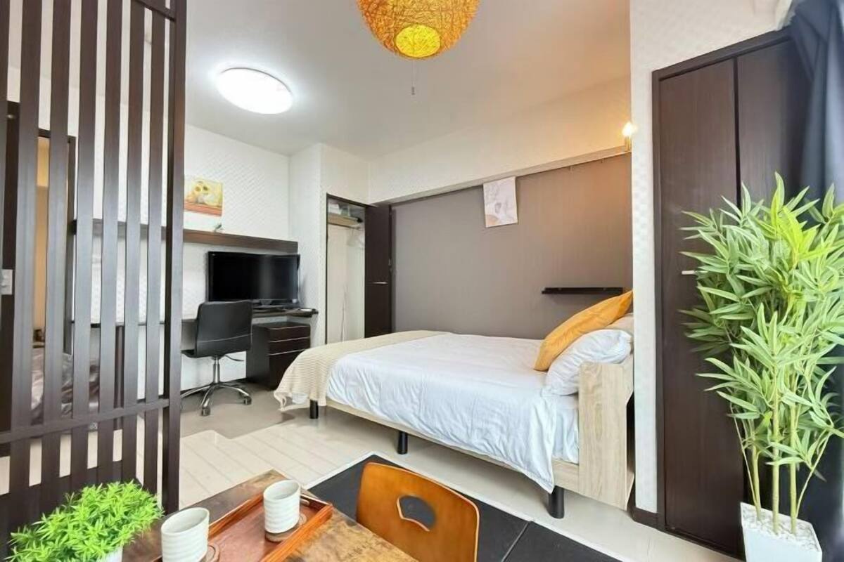 A modern hotel room with a bed, desk, chair, and a large potted plant.