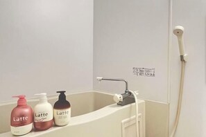 Une salle de bain avec une baignoire, un pommeau de douche à main et trois bouteilles de gel douche étiquetées « Latte ».