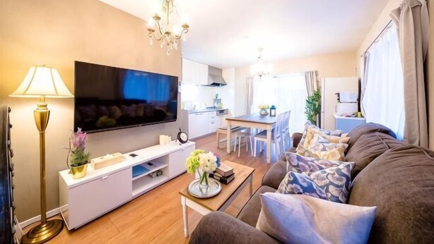 Una sala de estar moderna con un televisor de pantalla plana, un sofá, una mesa de centro y un comedor al fondo.