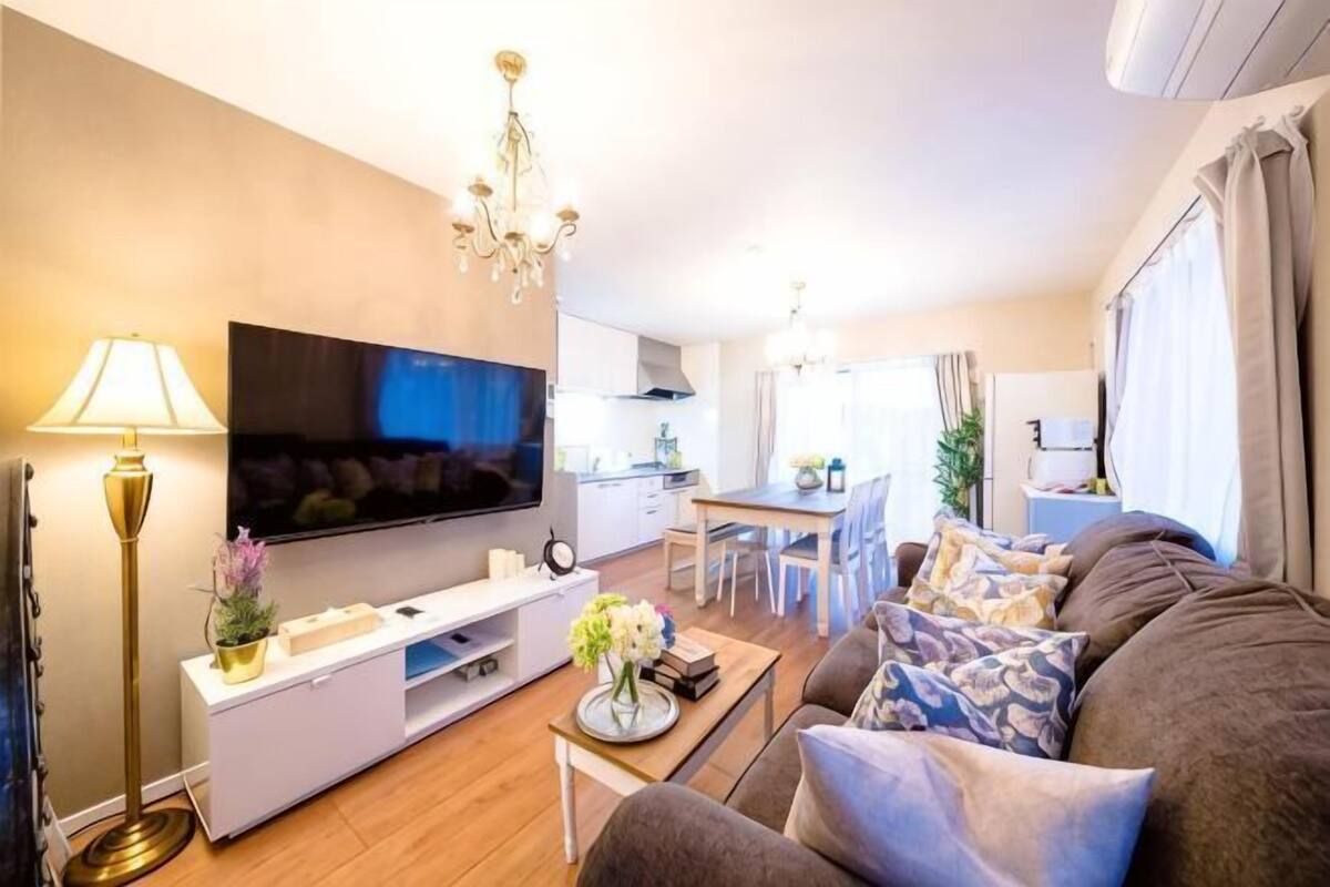 Un salon moderne avec un téléviseur à écran plat, un canapé, une table basse et un coin repas à l’arrière-plan.