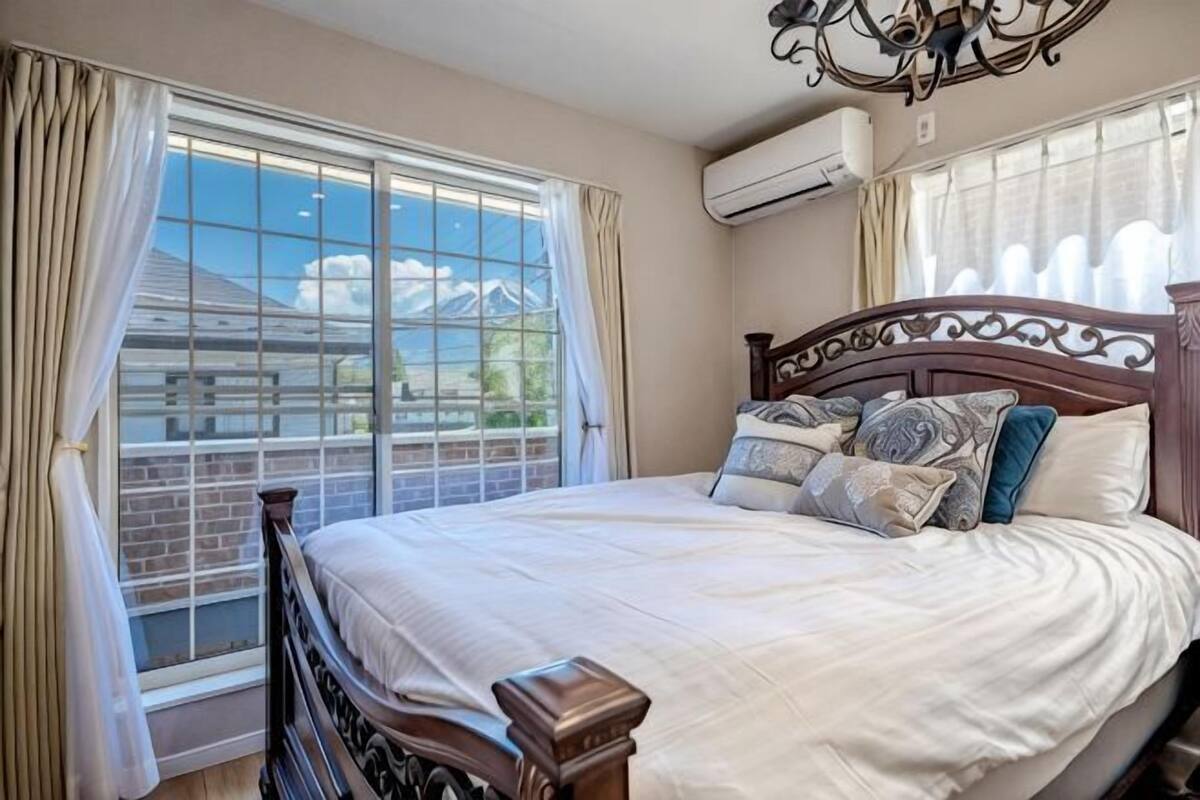 Une chambre à coucher avec un grand lit, une tête de lit en bois et une vue sur une maison par la fenêtre.