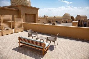 Una terraza en la azotea con un banco de madera, dos sillas y una mesa.