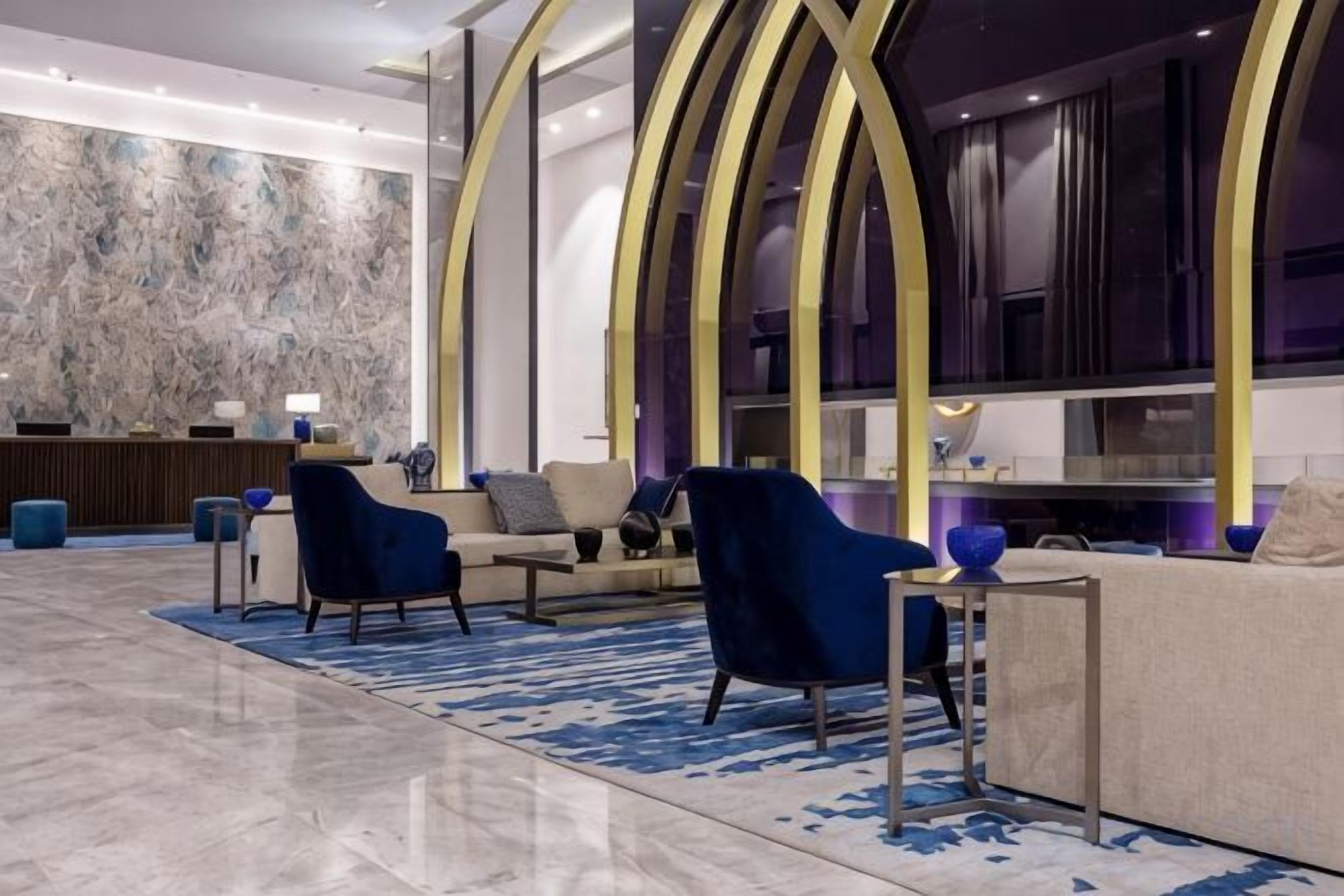 Un vestíbulo moderno con un mostrador de recepción de mármol, zona de estar con sofás y sillones, y un ventanal con vistas.