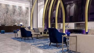 Un vestíbulo moderno con un mostrador de recepción de mármol, zona de estar con sofás y sillones, y un ventanal con vistas.
