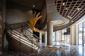 Eine großzügige Lobby mit einer imposanten Treppe, einer großen, goldenen Skulptur und einem modernen Deckenstil.