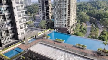 Edifício residencial com piscina no terraço, rodeado por áreas verdes e outros arranha-céus.