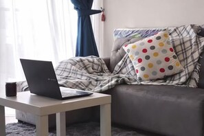 A living room with a sofa, a laptop on a small table, and a window with curtains. - D'Pristine Homestay ByStay (Iskandar Puteri)