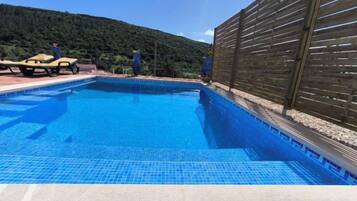 A swimming pool with a wooden fence and a mountain backdrop.