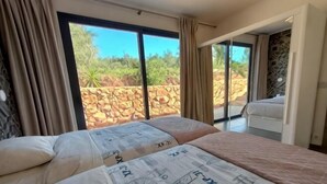 Un dormitorio con una cama grande, un balcón con vistas a un paisaje rocoso y una puerta corredera que da a otra habitación.