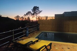 Une piscine avec des chaises longues, une clôture en bois et un arbre en arrière-plan.