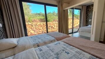 A bedroom with a large bed, a sliding glass door leading to a balcony, and a stone wall outside.