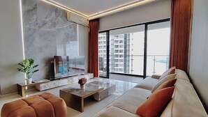 A modern living room with a sofa, ottoman, and a flat-screen TV. - Astonishing Ocean View 4 Bedrooms Huge Balcony 2 Car Park (Johor Bahru)