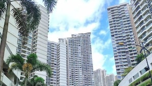 A high-rise residential building with multiple balconies, surrounded by palm trees and other greenery. - Astonishing Ocean View 4 Bedrooms Huge Balcony 2 Car Park (Johor Bahru)