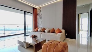 A modern living room with a sofa, ottoman, and coffee table, large windows, and a balcony. - Astonishing Ocean View 4 Bedrooms Huge Balcony 2 Car Park (Johor Bahru)