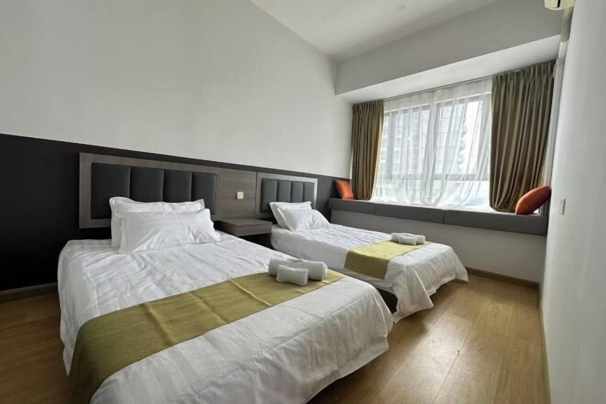 Una camera d'albergo con due letti, una finestra con tende e un pavimento in legno.