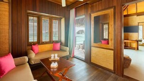Una habitación acogedora con techo de madera, un sofá con cojines rosados, una mesa de madera con zapatillas y vistas a un área exterior a través de un ventanal.