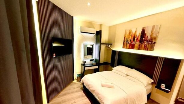 A hotel room with a bed, a flat-screen TV, a desk with a chair, a mirror, and a painting on the wall. - Hota Inn Limbang (Limbang)