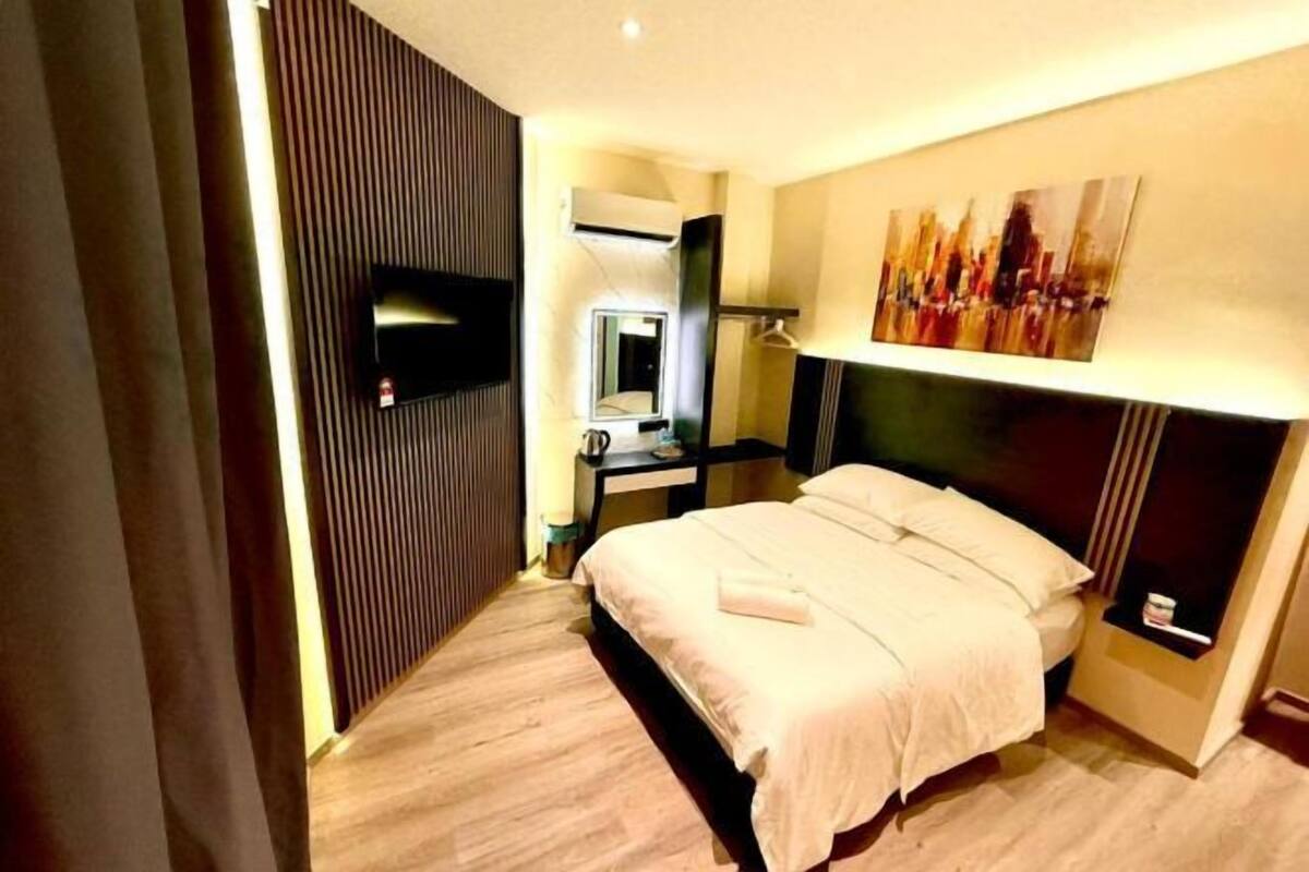 A hotel room with a bed, a flat-screen TV, a desk with a chair, a mirror, and a painting on the wall.
