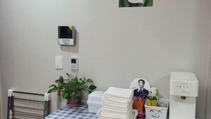 A hotel room with a checkered tablecloth, a stack of white towels, a water dispenser, a small potted plant, a picture frame, and a wall-mounted thermostat. - Incheon Airport ANN Guesthouse (Incheon)