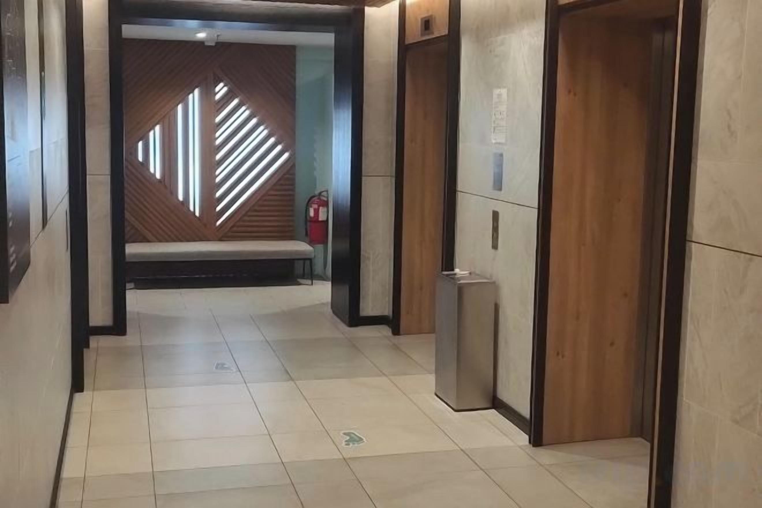 A hallway with a bench, a fire extinguisher, and an elevator.