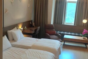 Una camera d'albergo con due letti, una scrivania, una sedia, una panca e una finestra con tende.