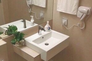 Un bagno con un lavandino bianco, uno specchio, una pianta, un asciugacapelli e un asciugamano appeso al muro.