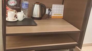 A hotel room with a wooden desk, a coffee maker, a water bottle, and a calendar.