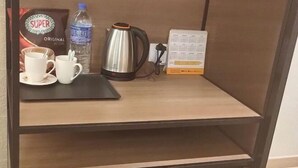 Ένα ξύλινο ράφι με μια καφετιέρα, φλιτζάνια, ένα μπουκάλι νερό και ένα ημερολόγιο.