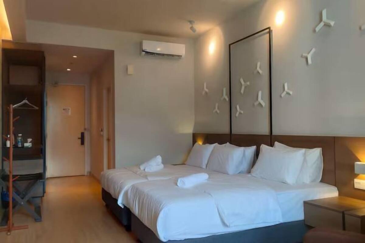 A hotel room with a bed, a bedside table, an air conditioning unit, and a wardrobe.