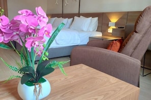 A hotel room with a bed, a brown armchair, a wooden coffee table, and a potted plant with pink flowers. - Windmills Upon Hills Hotels & Residences Genting Highland (Genting Highlands)