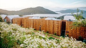 A wooden building with a green entrance, surrounded by white flowers and a mountainous backdrop. - Phutawan monjam (Mae Rim)