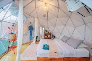 A dome-shaped tent with a bed, a small table with a basket of flowers, and a hanging light fixture. - Phutawan monjam (Mae Rim)