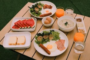 Una mesa preparada para el desayuno, con huevos, tocino, jamón, tostadas y una variedad de frutas y verduras.