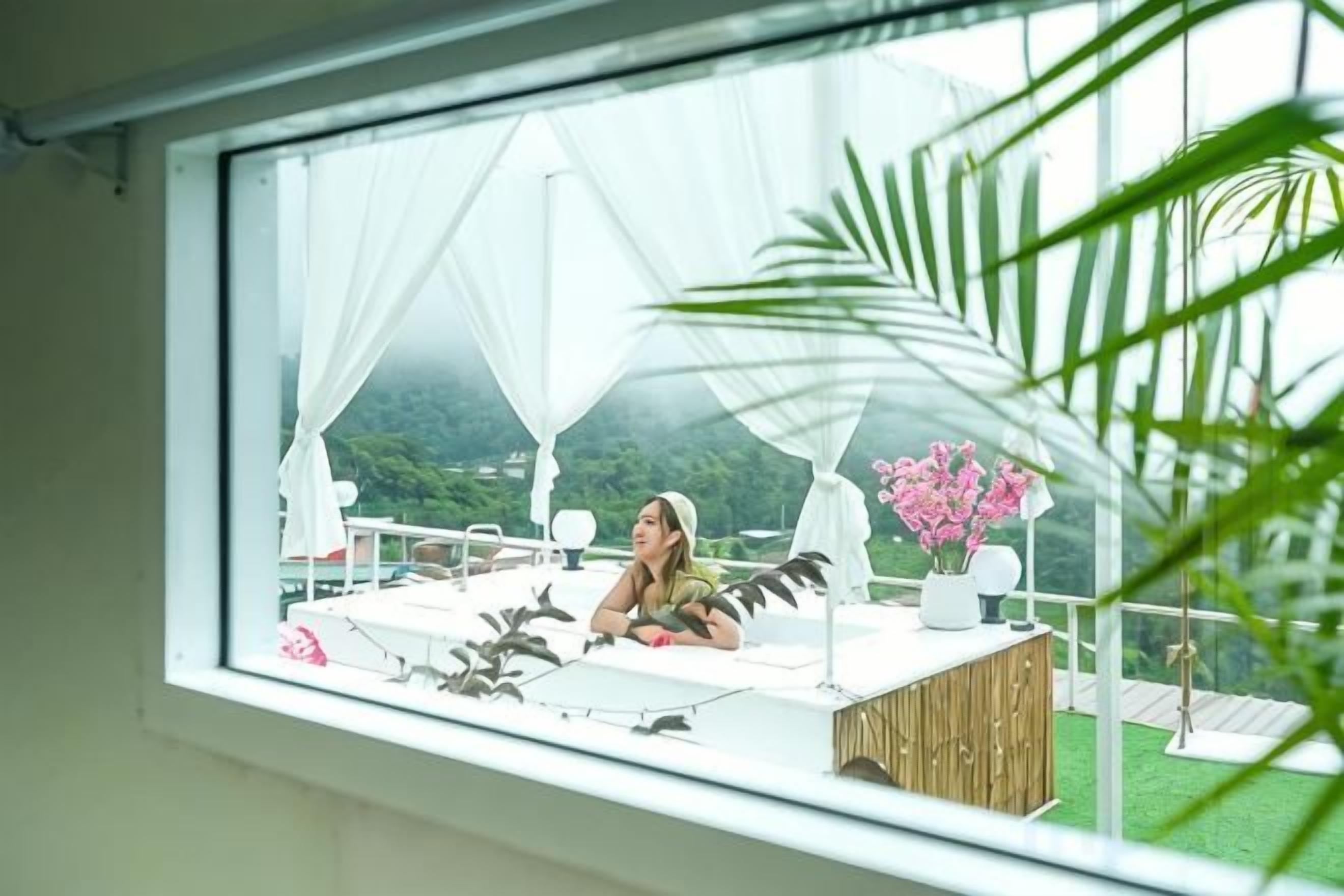 Una habitación con un ventanal grande, una cama, una mesita de noche y vistas a zonas verdes.