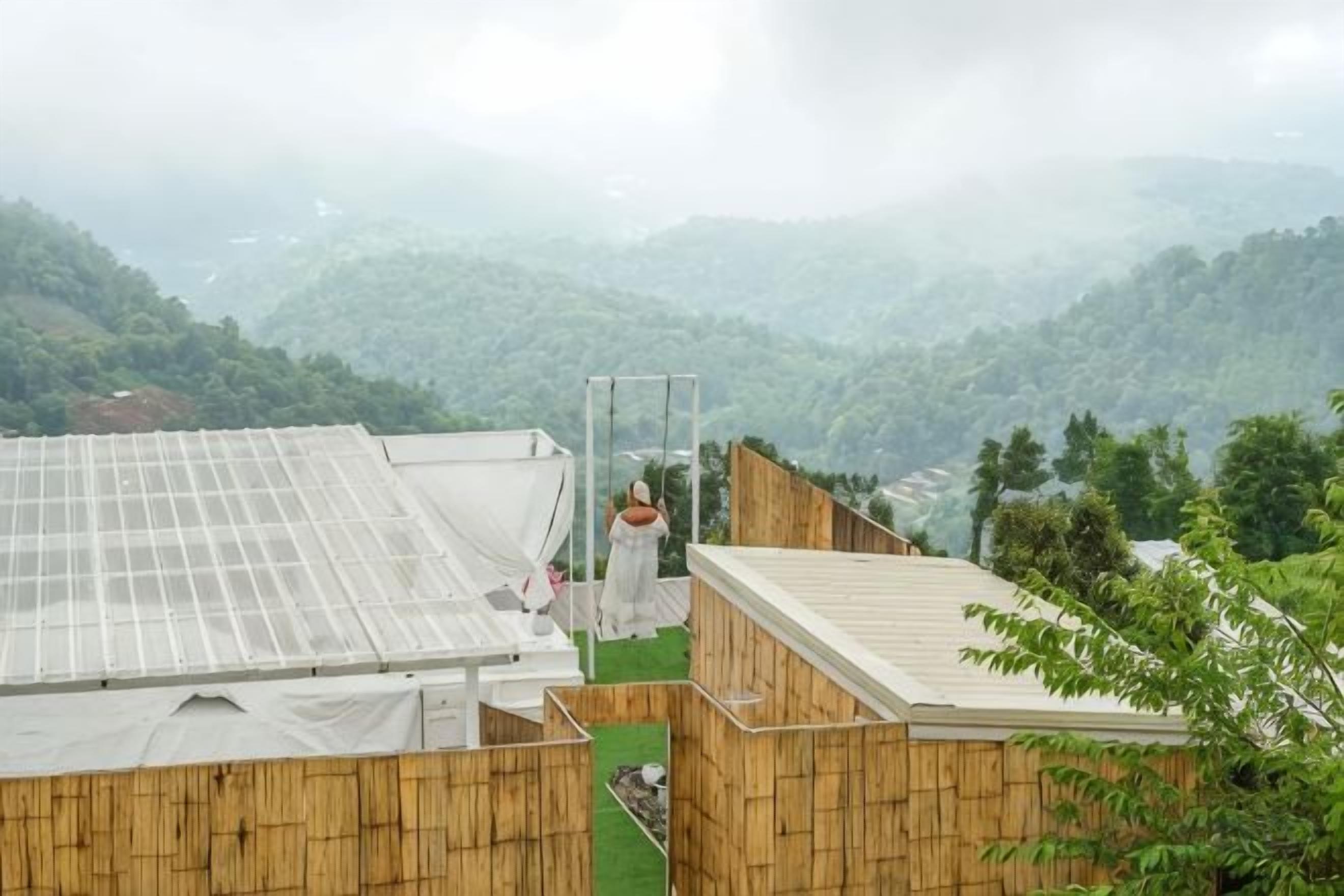 Una habitación con vistas a un paisaje montañoso, una estructura de bambú y un panel de vidrio.