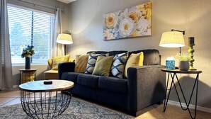 Een woonkamer met een bank, twee bijzettafels, een ronde salontafel en een schilderij aan de muur.