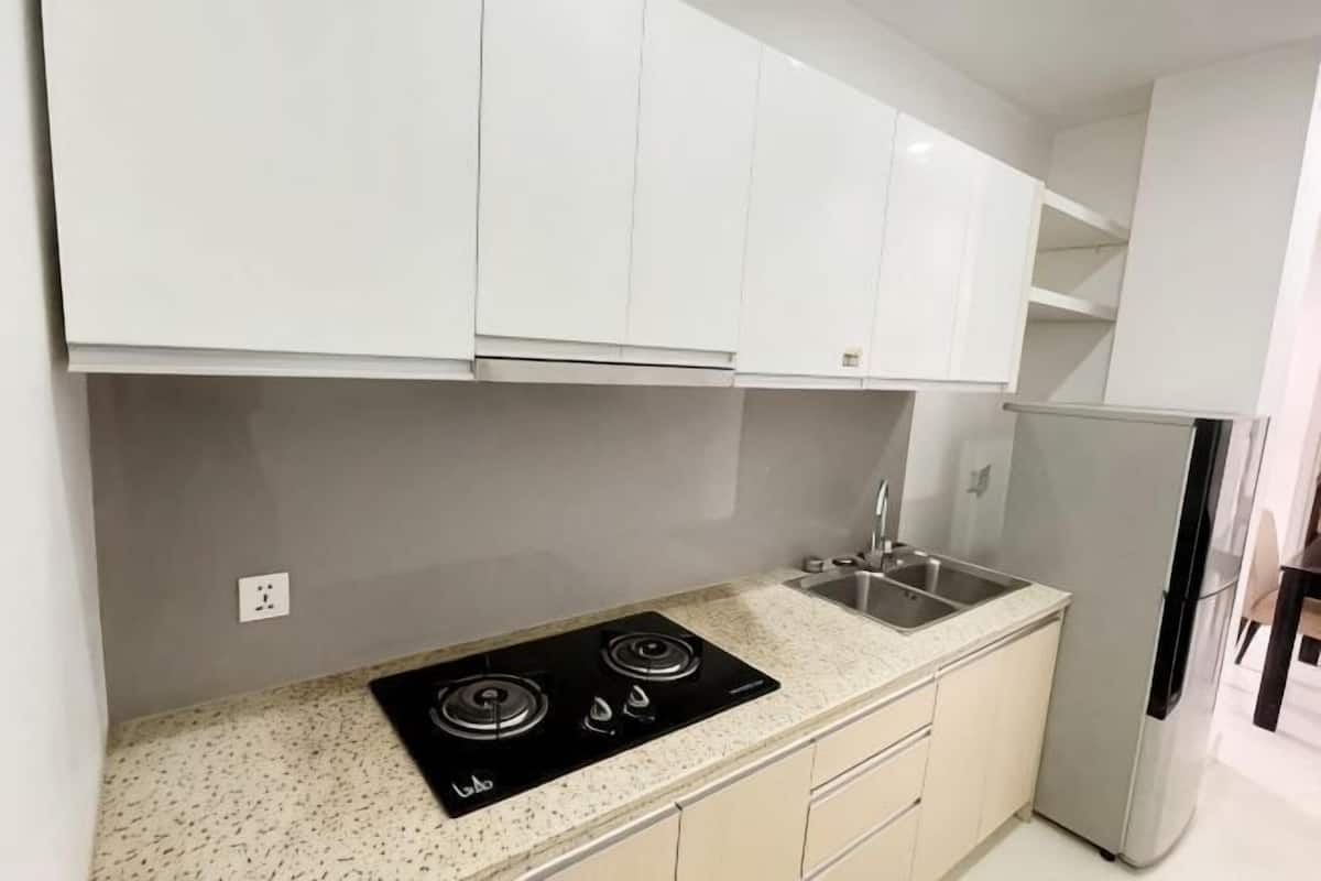 A kitchen with white cabinets, a black stove, a sink, and a refrigerator.