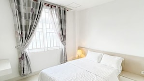 A bedroom with a bed, curtains, a bedside table, and a nightstand. - Daily Apartment & Residence (Phnom Penh)