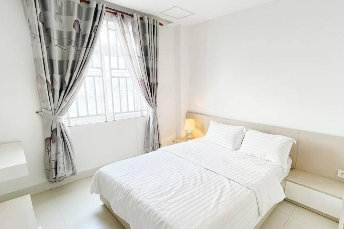 Ein Schlafzimmer mit Bett, Vorhängen, einem Nachttisch und einem Beistelltisch.