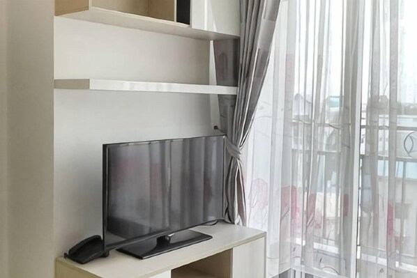 Una habitación con escritorio, televisión de pantalla plana y ventana con cortinas.