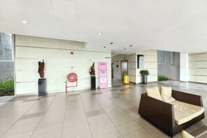 Un hall d’entrée spacieux au design moderne, comprenant un comptoir d’accueil, un coin salon avec un canapé et un panneau d’information fixé au mur.