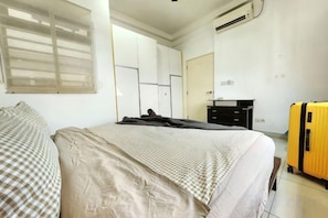 Une chambre à coucher avec un lit, une valise, un bureau et une armoire.