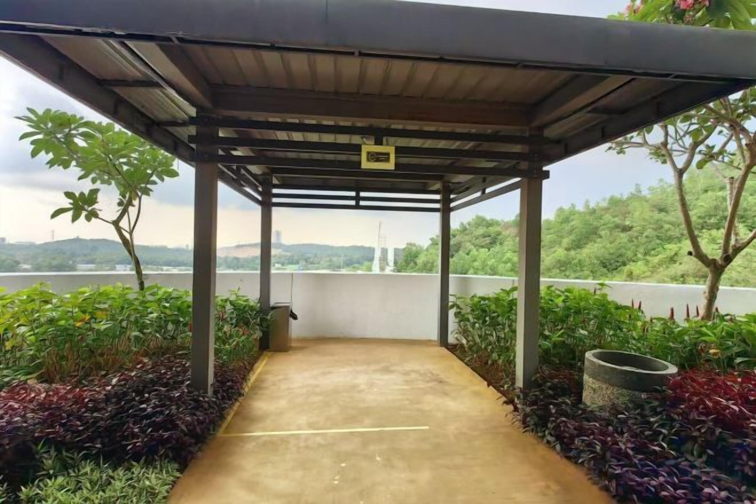 A covered outdoor area with a concrete path, surrounded by plants and a view of a body of water.