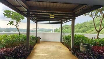 A covered outdoor area with a concrete path, surrounded by plants and a view of a body of water.