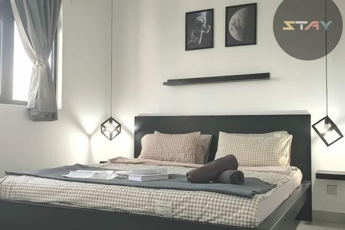 Ein modernes Schlafzimmer mit einem Bett, karierten Bettwäsche, zwei gerahmten Bildern, einem Regal und einem runden Logo an der Wand.