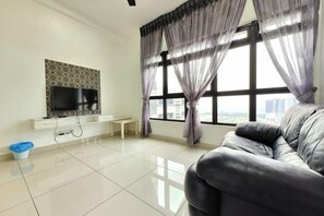Ein Wohnzimmer mit Flachbildfernseher, einer Couch, einer Bank und einem Fenster mit Vorhängen.