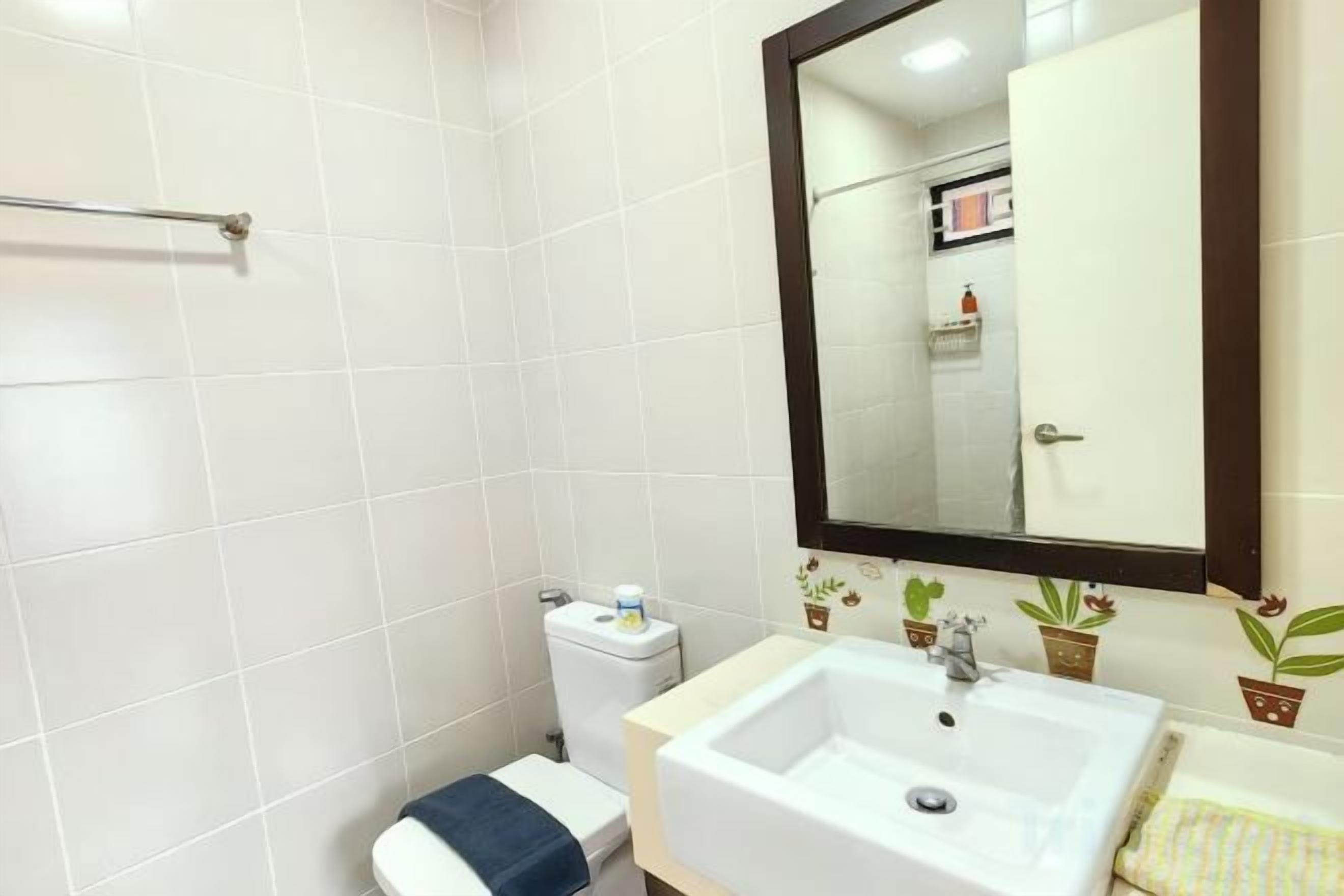 A bathroom with white tiles, a sink, a mirror, and a toilet.