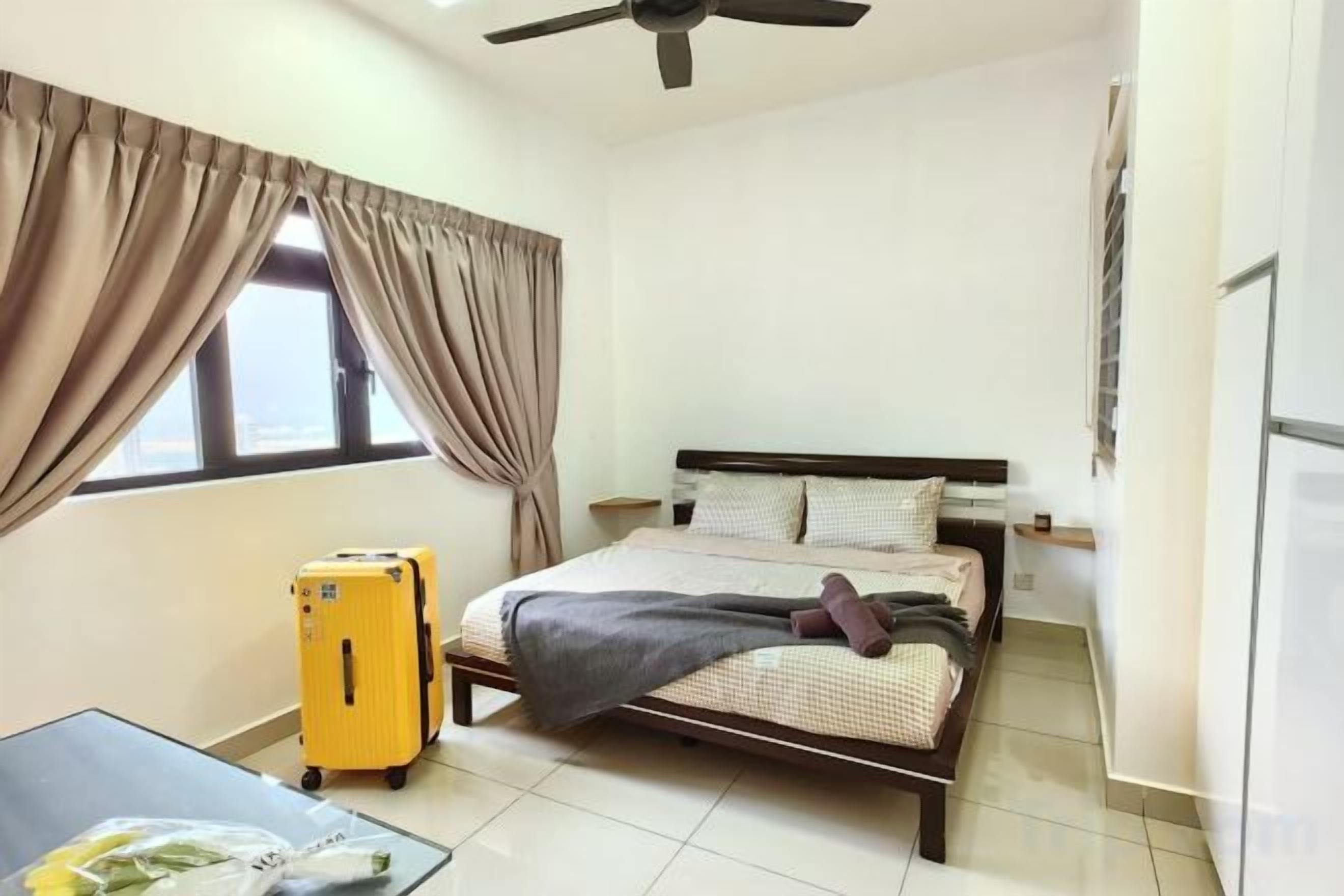 Un dormitorio con cama, cortinas, maleta, ventilador de techo y ventana.