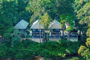 A row of three modern, triangular-roofed buildings surrounded by dense tropical forest.